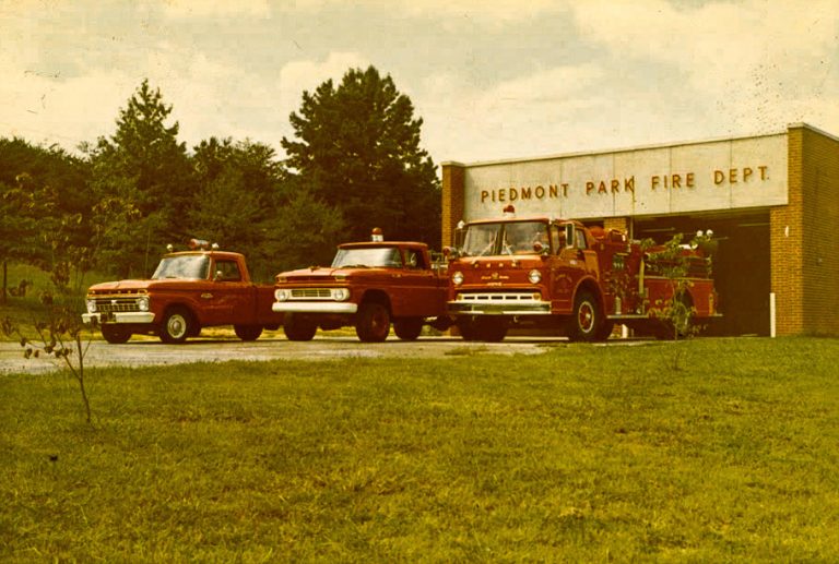 Vintage photograph of three fire trucks parked outside a brick fire station labeled "Piedmont Park Fire Dept." The trucks are bright red, and the surrounding area is green with trees and grass. Dated September 1969.